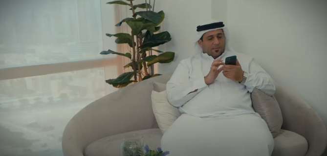 A man is seated on a sofa using a smartphone